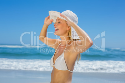 Smiling blonde in white bikini and sunhat on the beach