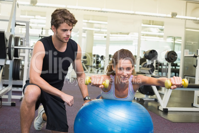 Trainer watching client balance on exercise ball with dumbbells