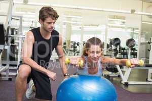 Trainer watching client balance on exercise ball with dumbbells