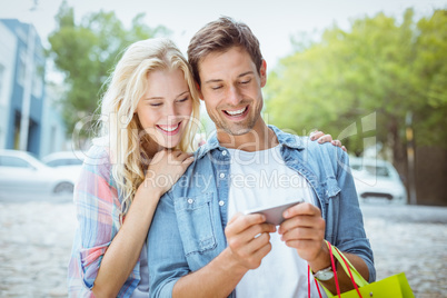 Hip young couple looking at smartphone on shopping trip