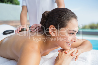 Happy brunette getting a hot stone massage poolside