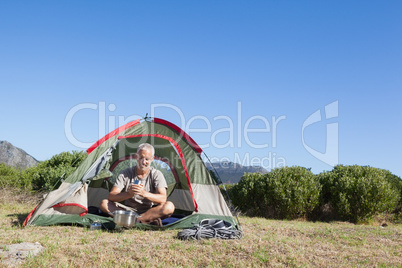 Happy camper holding mug outside his tent