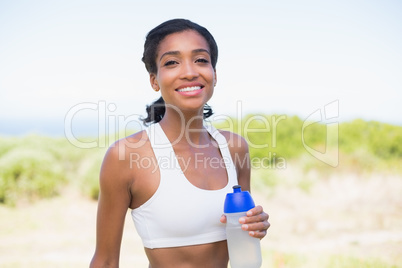 Fit woman holding sports bottle smiling at camera