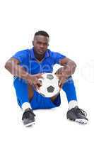 Football player in blue sitting with ball