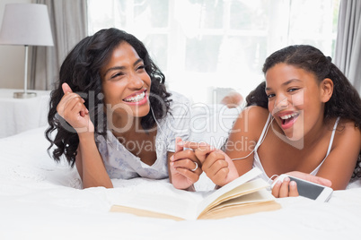 Mother and daughter reading book and listening to music together