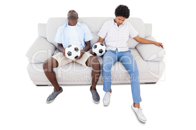 Distraught football fans sitting on the couch with balls