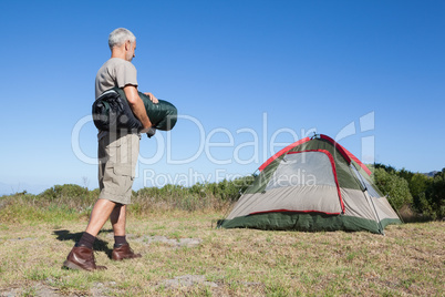 Happy camper walking towards his tent holding sleeping bag