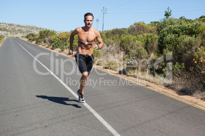 Athletic man jogging on open road with monitor around chest