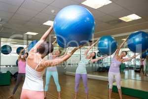 Fitness class holding up exercise balls in studio