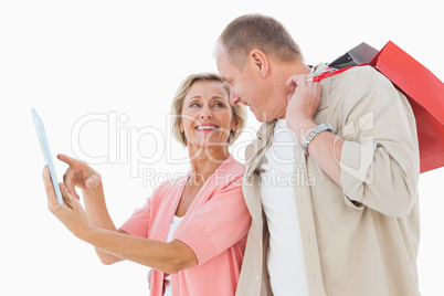 Smiling older couple holding shopping bags looking at tablet pc