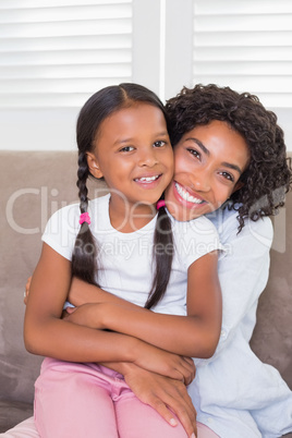 Pretty mother sitting on the couch with her daughter smiling at