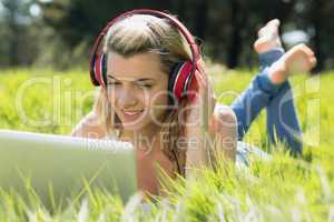 Pretty blonde lying on grass using laptop listening to music