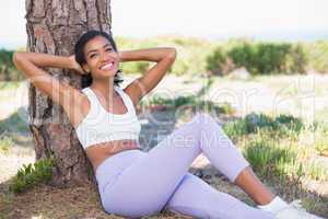 Fit woman sitting against tree smiling at camera