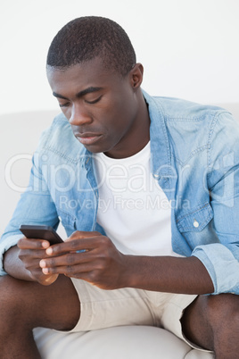 Casual man sitting on sofa texting on phone