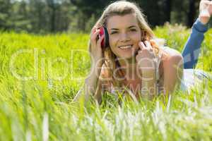 Pretty blonde lying on grass with headphones around neck