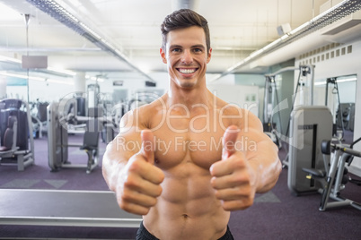 Smiling muscular man giving thumbs up in gym