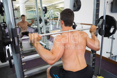 Shirtless muscular man lifting barbell in gym