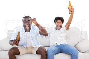 Ecstatic sports fans sitting on the couch with beers