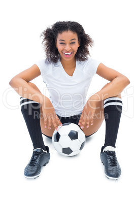 Pretty football player in white sitting on floor with ball