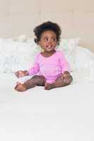 Baby girl in pink babygro sitting on bed