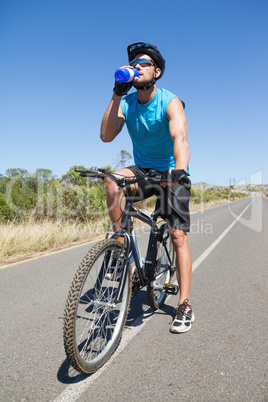 Handsome cyclist taking a break on his bike drinking water