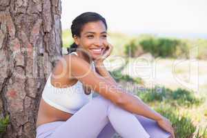 Fit woman sitting against tree smiling