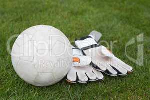 Goalkeeping gloves and football on pitch