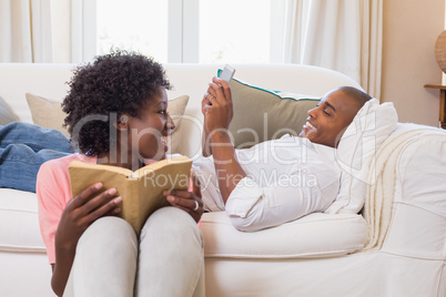 Cute couple relaxing reading book and using smartphone