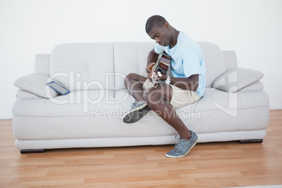 Casual man sitting on sofa playing the guitar with tablet pc