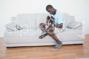 Casual man sitting on sofa playing the guitar with tablet pc