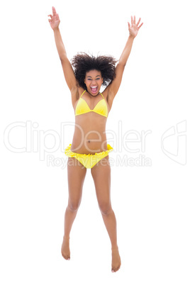 Fit girl in yellow bikini jumping and smiling at camera