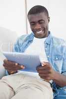 Casual man lying on sofa using his tablet pc