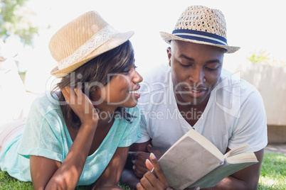 Happy couple lying in garden together reading book