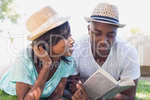 Happy couple lying in garden together reading book