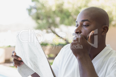 Handsome man in bathrobe reading newspaper outside