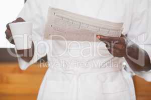 Man in bathrobe holding coffee and newspaper