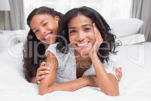 Pretty woman lying on bed with her daughter smiling at camera