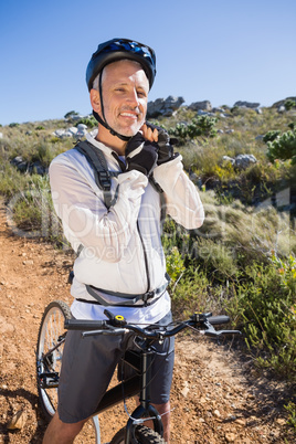 Fit cyclist adjusting helmet strap on country terrain smiling at