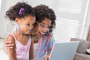 Cute daughter using laptop at desk with mother