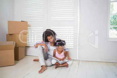 Mother and daughter sitting on the floor reading storybook i