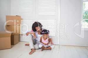 Mother and daughter sitting on the floor reading storybook i