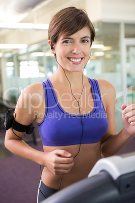 Fit brunette running on the treadmill listening to music