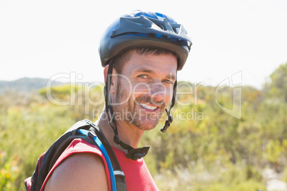 Fit cyclist smiling at the camera on country terrain