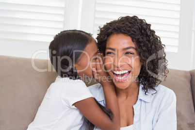 Pretty mother sitting on the couch with her daughter whispering