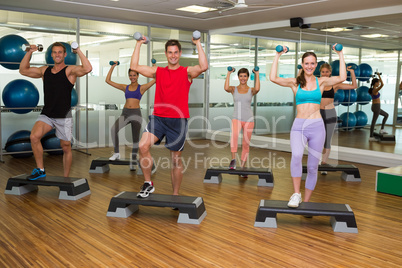 Fitness class doing step aerobics with dumbbells