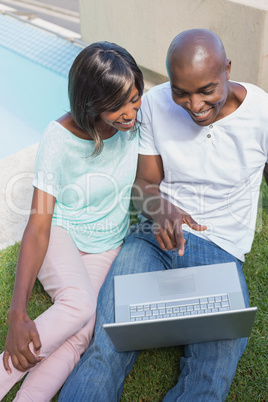 Happy couple sitting in garden using laptop together Happy couple sitting in garden using laptop together