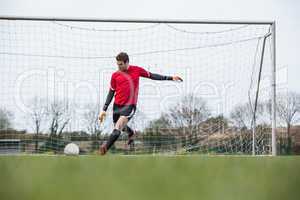 Goalkeeper in red kicking ball away from goal