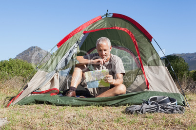 Happy camper looking at map sitting in his tent