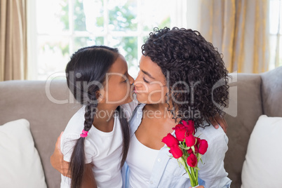 Pretty mother sitting on the couch kissing her daughter holding