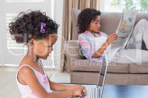 Cute daughter using laptop at desk with mother on couch